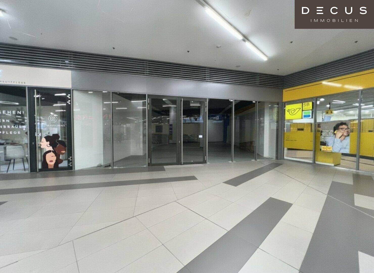Geräumiger Gewerberaum mit breiter Glasfront in einer Einkaufspassage, umgeben von anderen Geschäften.