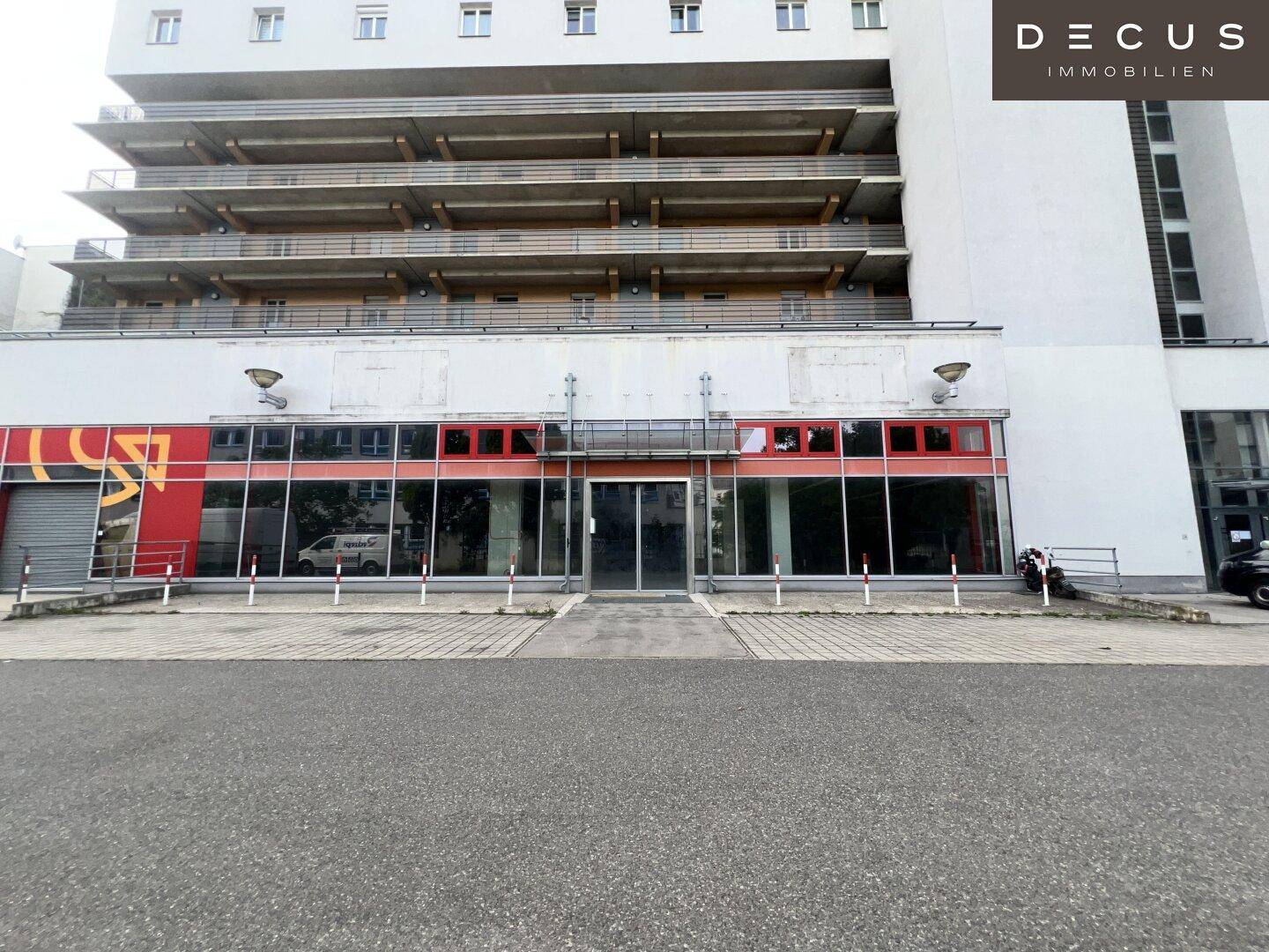 Gesamtansicht der Geschäftsfassade mit darüberliegenden Balkonen und einem großen Parkplatz davor.