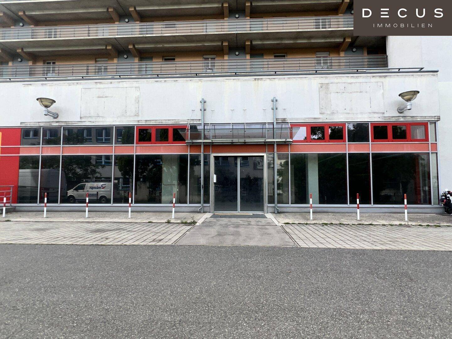 Weitwinkelansicht der Geschäftsfront mit roten Akzenten und einem mehrstöckigen Gebäude im Hintergrund.