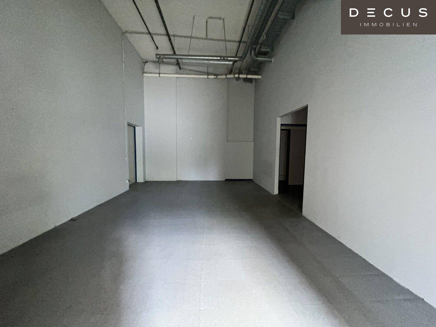 Langer, schmaler Gewerbe- oder Lagerraum mit grauem Fliesenboden und sichtbaren Deckeninstallationen.