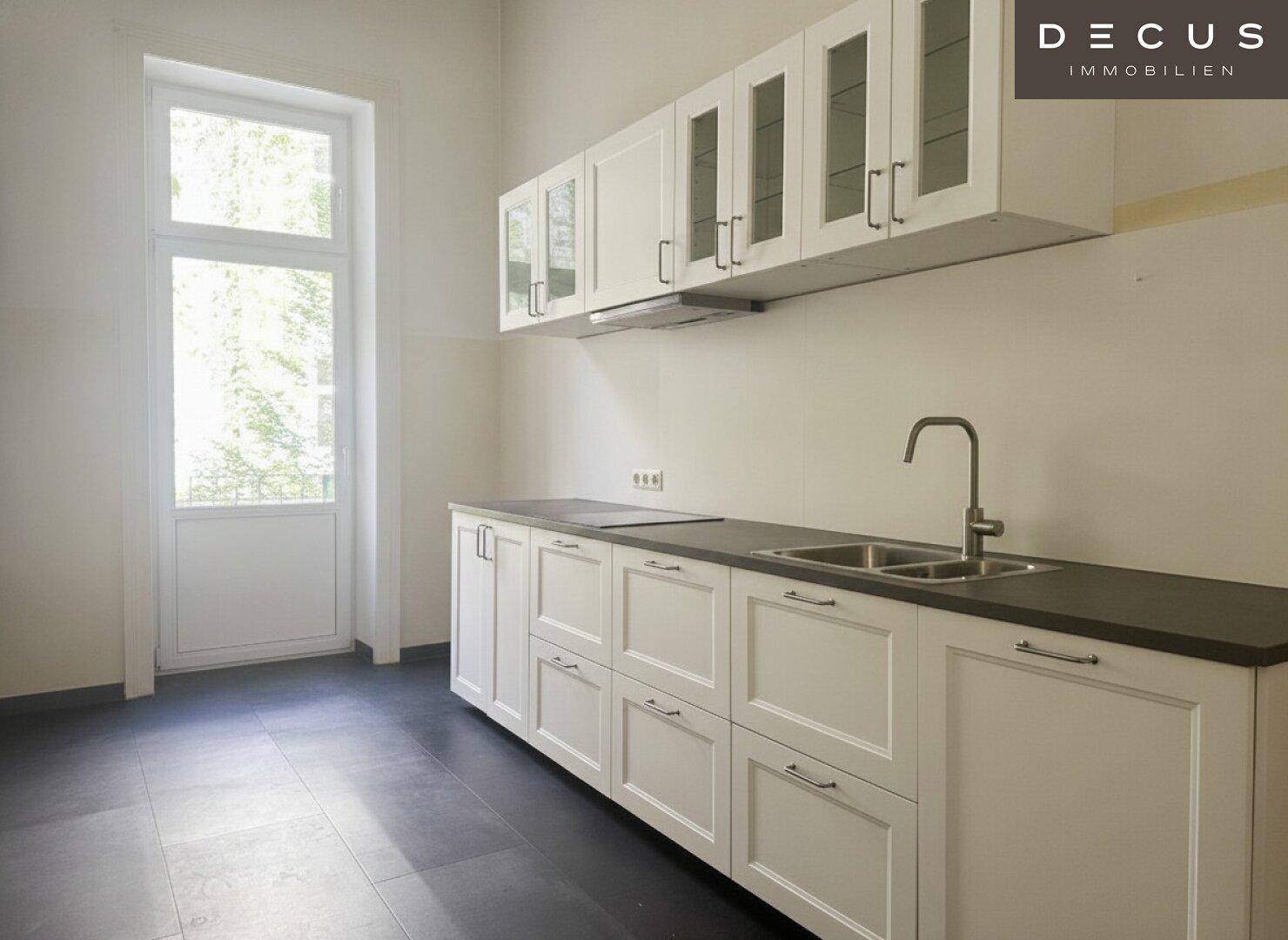 Helle Küche mit weißen Schränken, dunkler Arbeitsplatte und Zugang zu einem Balkon oder Garten.