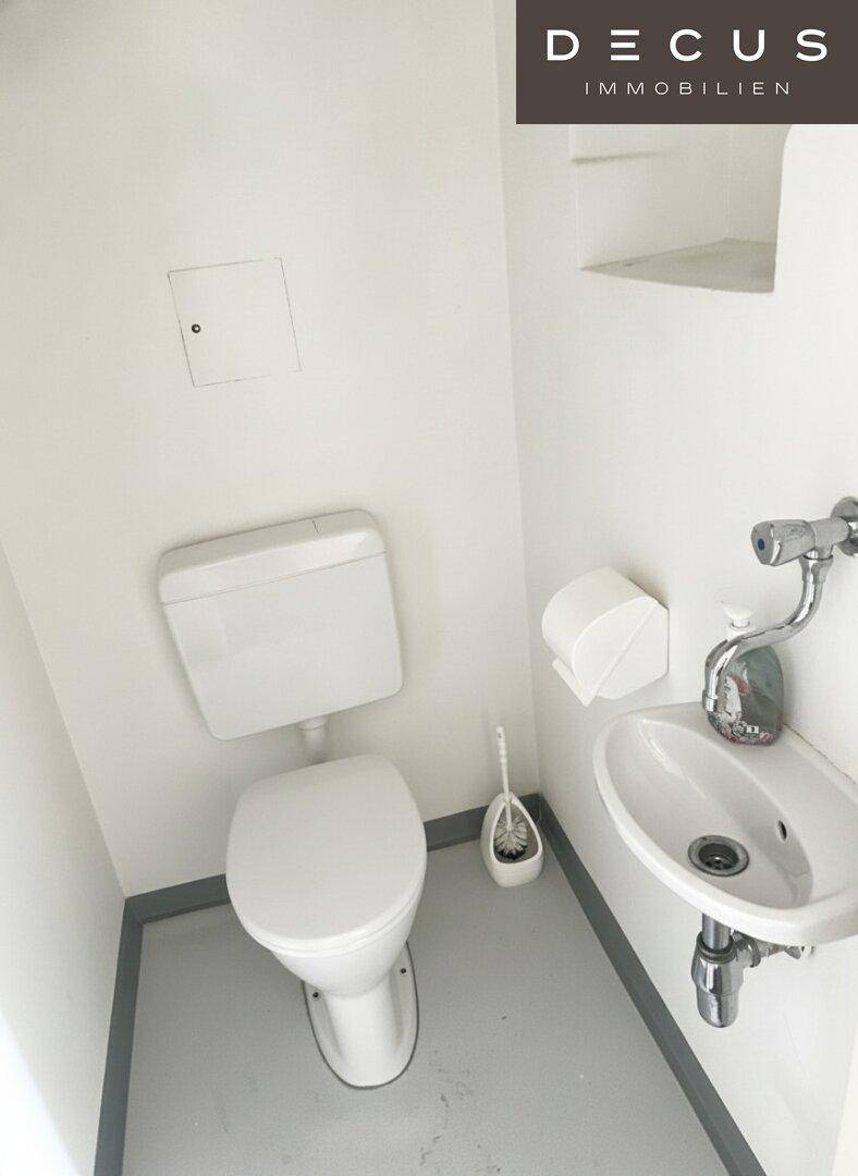 Kleines Gäste-WC mit weißer Toilette, Waschbecken und hellgrauem Fliesenboden.