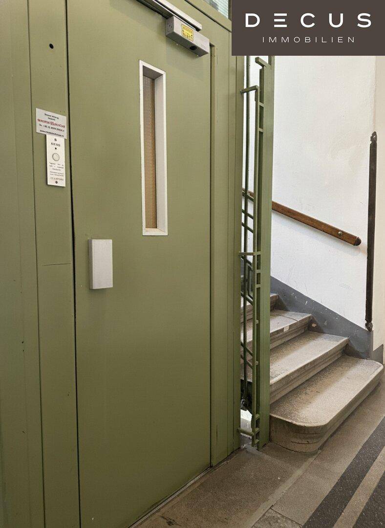 Historischer Treppenaufgang mit Aufzug und Holzgeländer in einem Altbau.