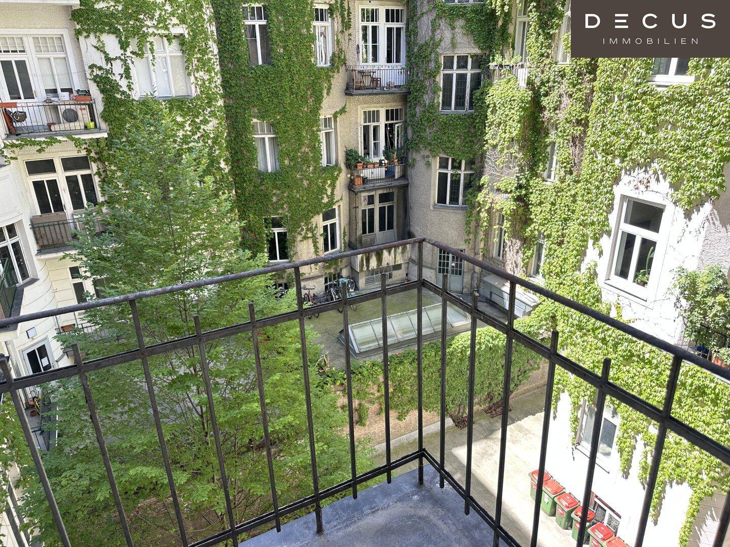 Blick vom Balkon auf einen begrünten Innenhof mit Rankpflanzen an den Fassaden.