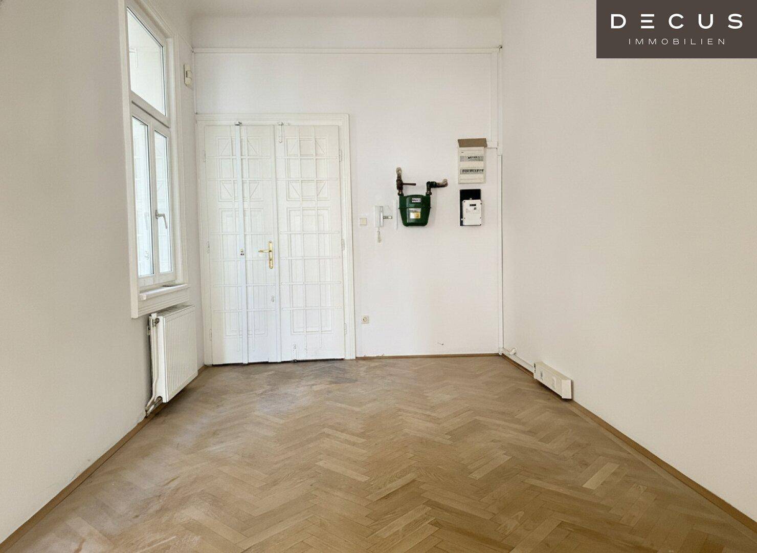 Flur mit Fischgrätparkett, einem Fenster und sichtbaren Zählerkästen an der Wand.