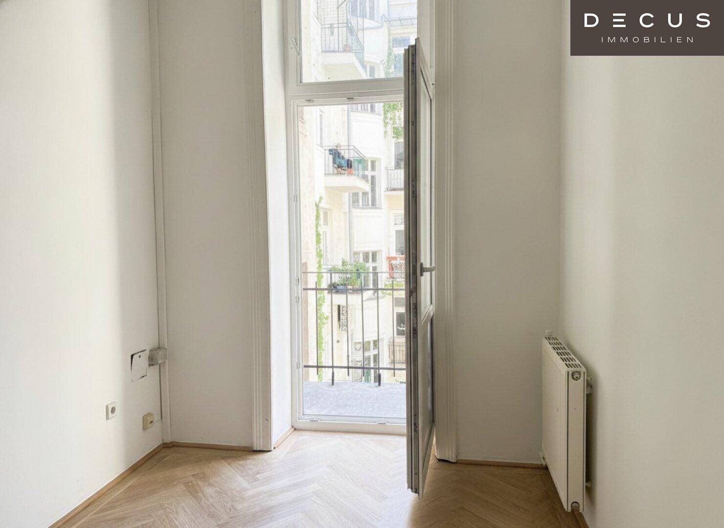Kleiner Raum mit Balkonzugang, Fischgrätparkett und einem Heizkörper unter dem Fenster.
