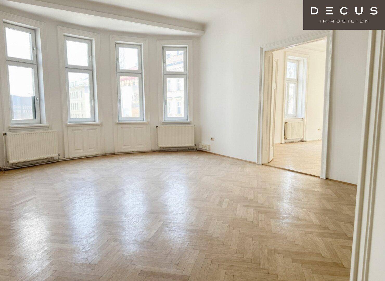 Großer, heller Wohnraum mit Erkerfenstern, Fischgrätparkett und hohen Decken.