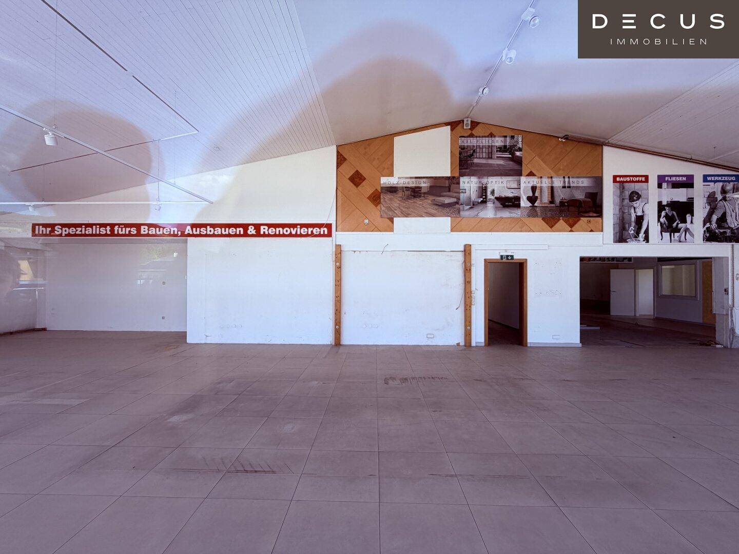 Großer, leerer Verkaufsraum mit hohen Decken, Fliesenboden und Werbeplakaten an den Wänden.
