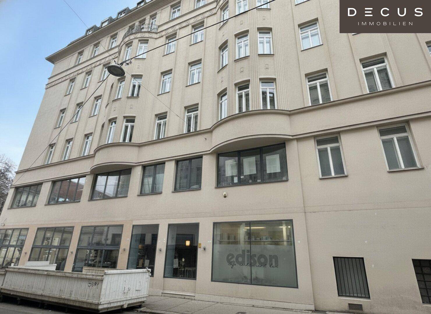 Klassisches Mehrfamilienhaus mit vielen Fenstern und Geschäften im Erdgeschoss in urbaner Umgebung.