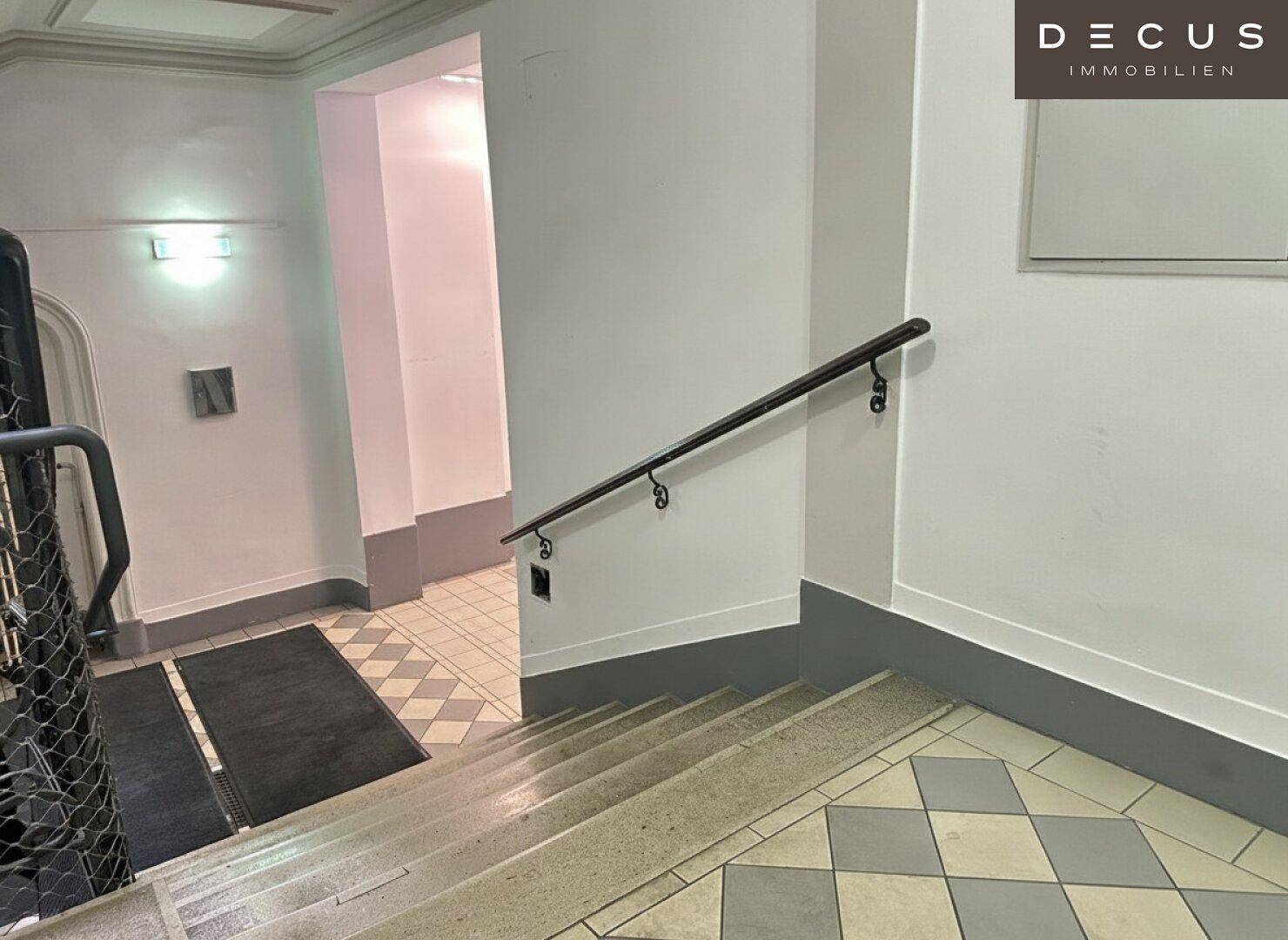 Treppenhaus eines Altbaus mit Handlauf und Fliesenboden, der zu den oberen Etagen führt.