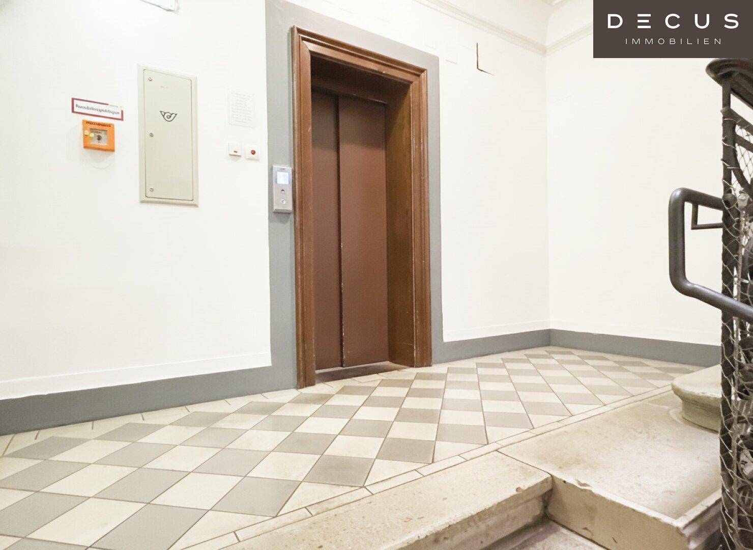 Heller Flur mit Aufzug, gemustertem Fliesenboden und Zugang zum Treppenhaus.