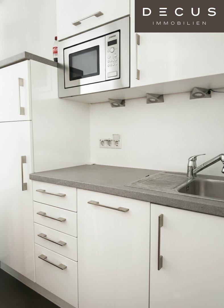 Moderne Küche mit weißen Hochglanzschränken, grauer Arbeitsplatte und eingebauter Mikrowelle.