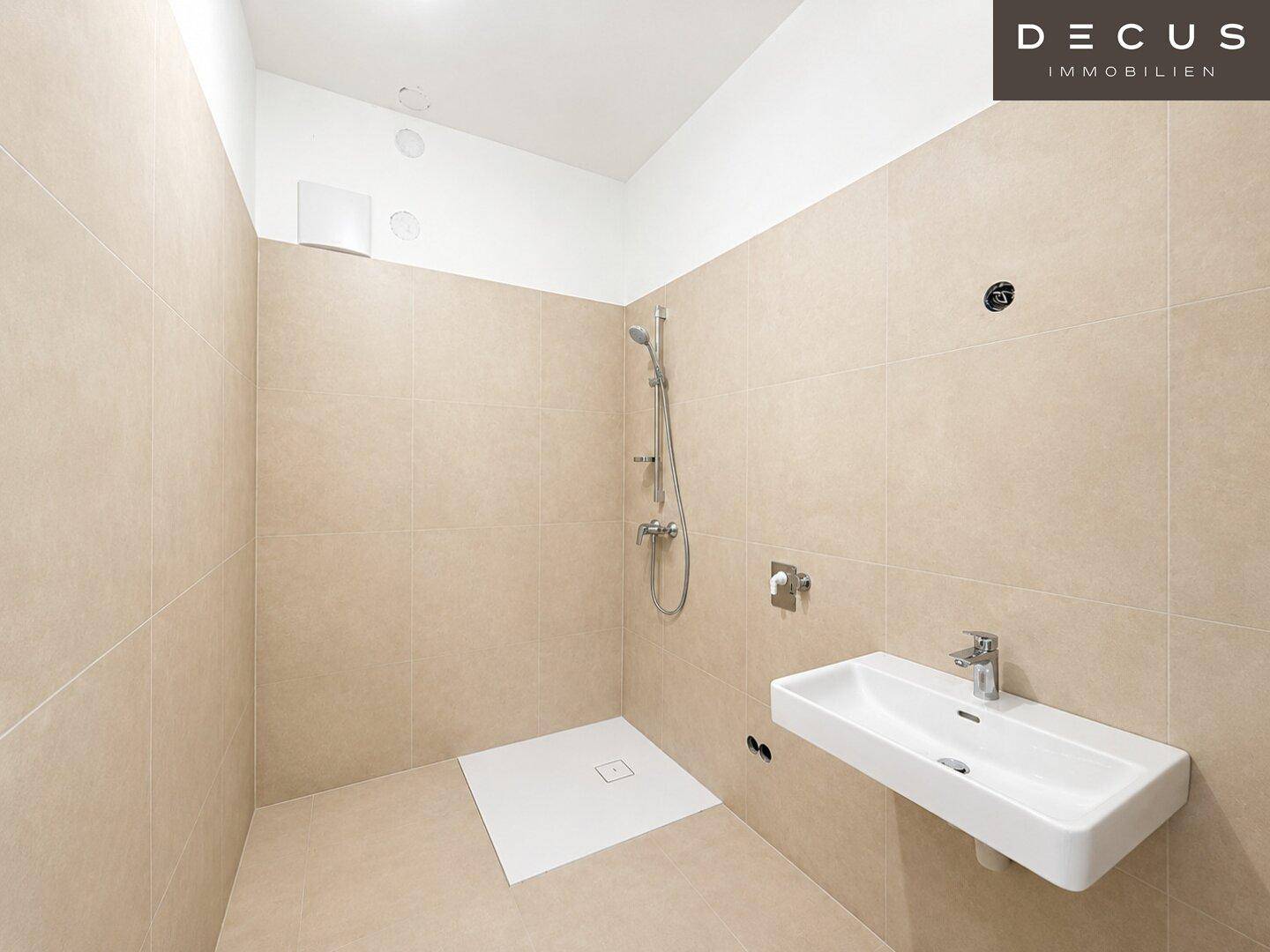 Leeres Badezimmer mit Duschbereich, Waschbecken und beigen Fliesen.
