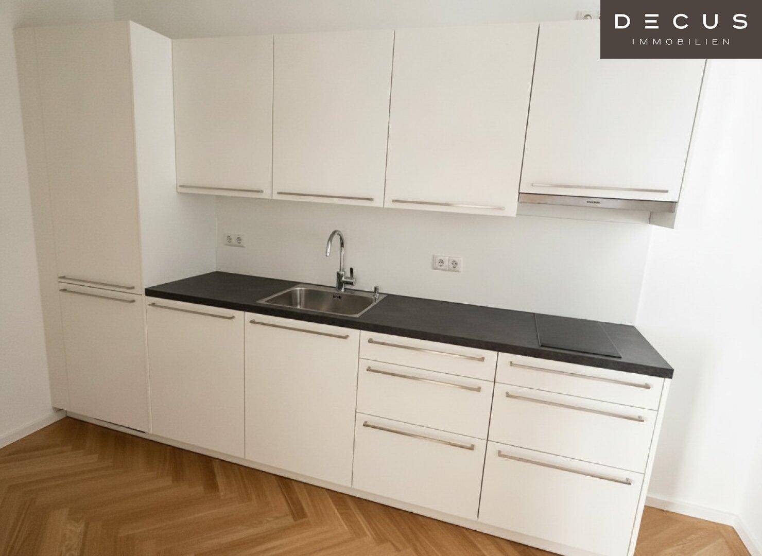 Moderne weiße Einbauküche mit dunkler Arbeitsplatte, Spüle und Induktionskochfeld.