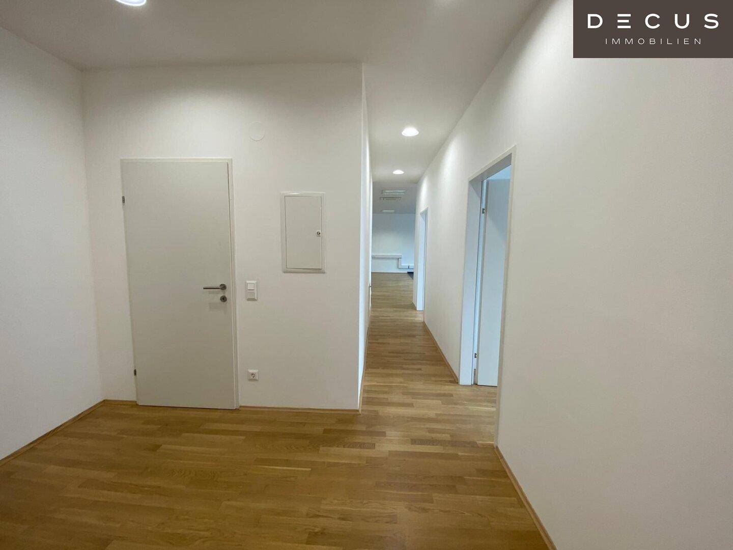 Heller Flur mit Holzboden und mehreren Türen, der verschiedene Bereiche des Gebäudes verbindet.