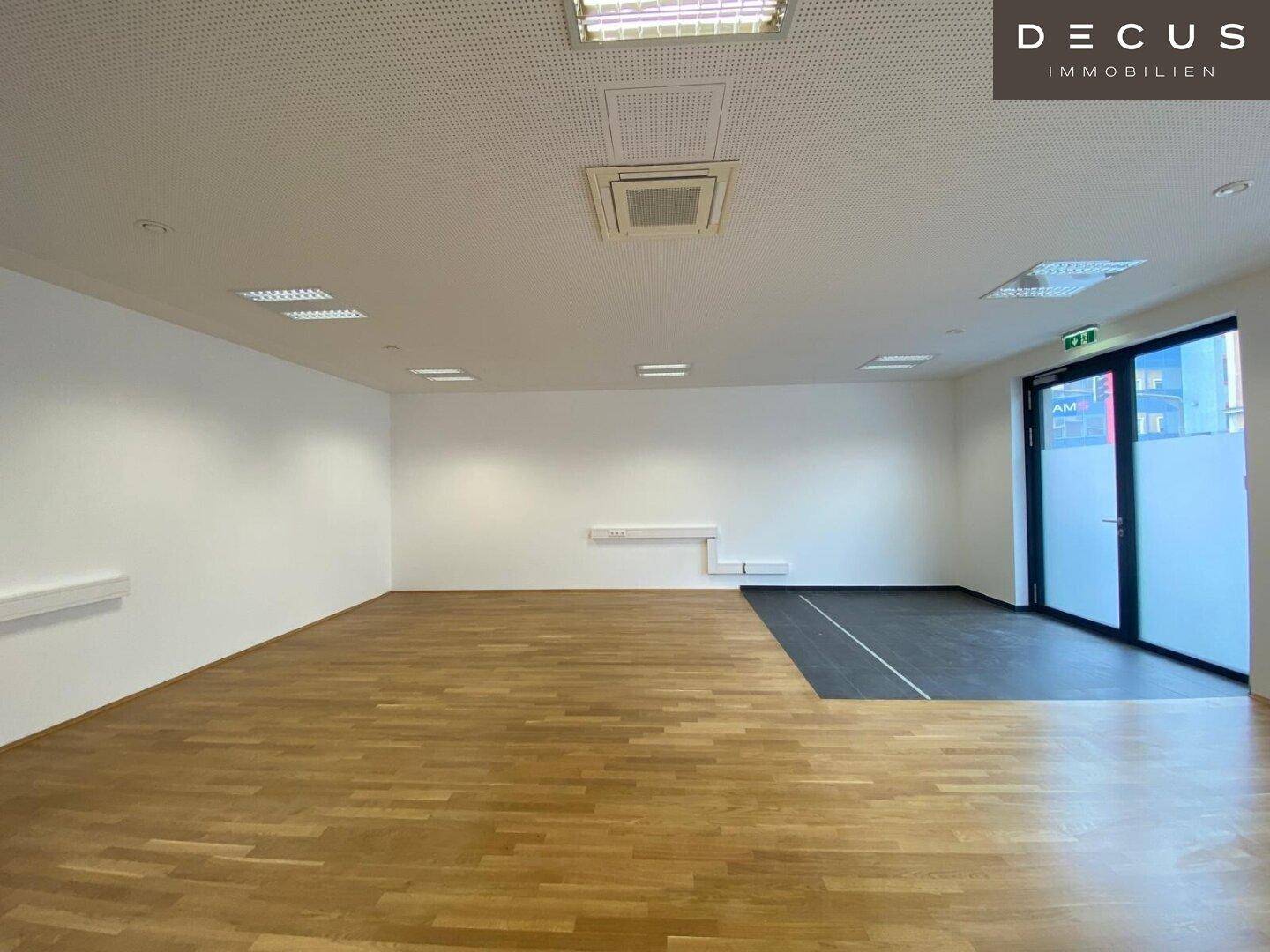 Geräumiger Büroraum mit Holzboden und einer großen Glastür, die viel Tageslicht hereinlässt.
