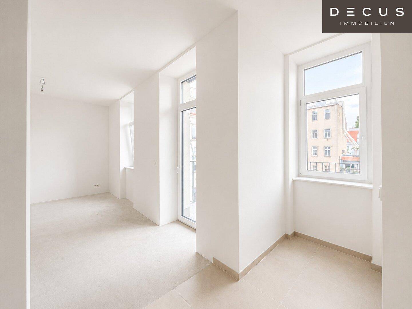 Heller, unmöblierter Raum mit großen Fenstern und Zugang zu einem französischen Balkon.