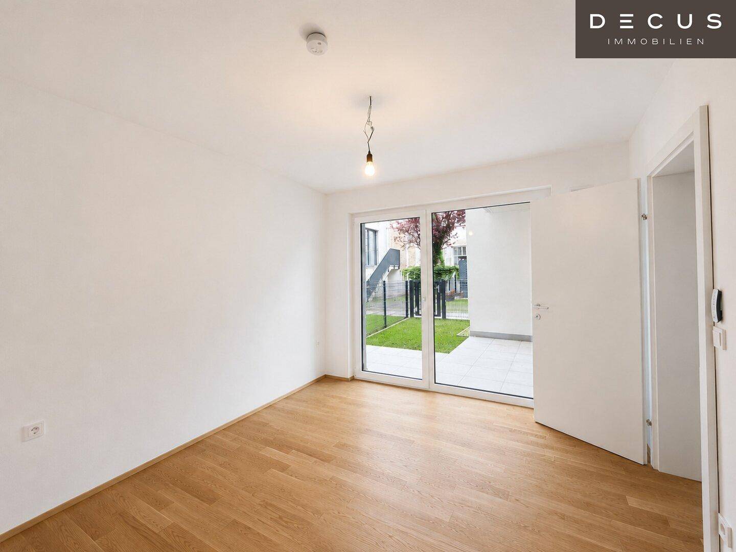 Helles, leeres Schlafzimmer mit Holzboden und großen Fenstern zum Außenbereich.
