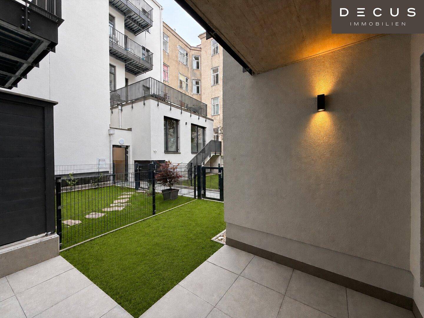 Ruhiger Innenhof mit gefliester Terrasse und gepflegter Rasenfläche, umgeben von Gebäuden.