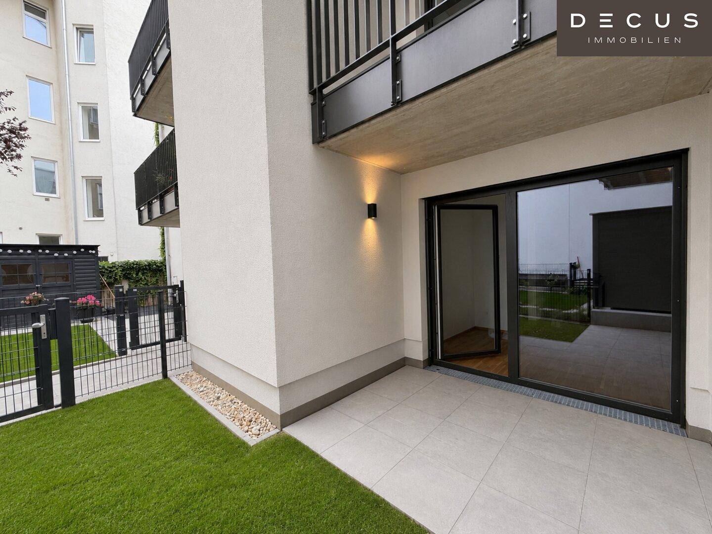 Geräumige, geflieste Terrasse mit angrenzender Rasenfläche und Blick auf die moderne Fassade.