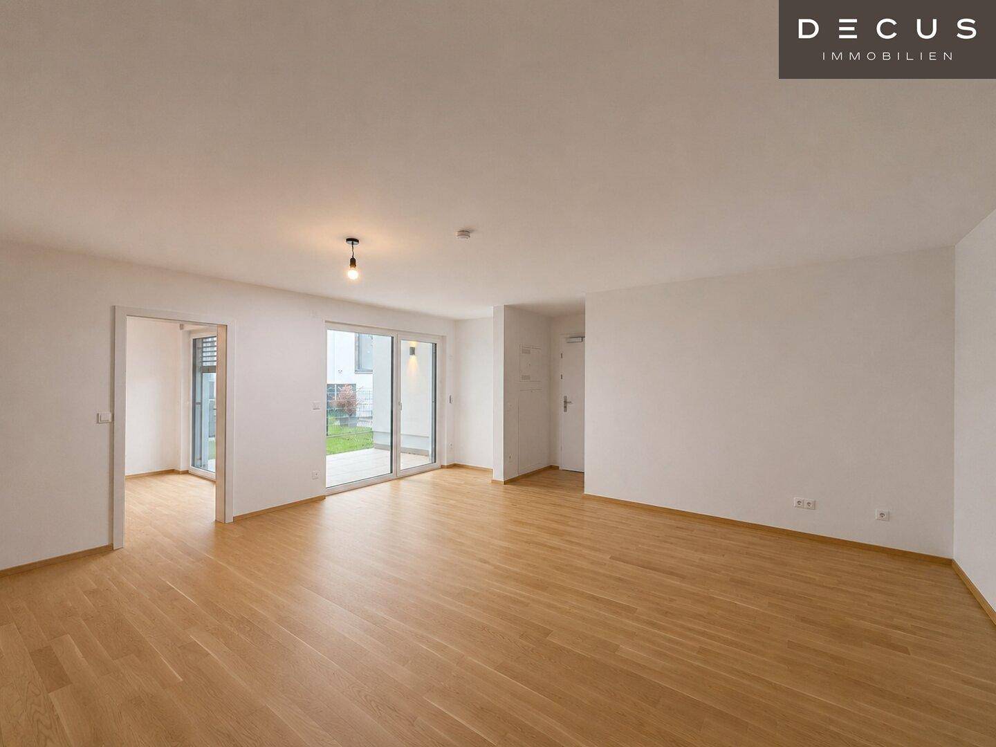 Geräumiges, leeres Wohnzimmer mit hellem Holzboden und großen Schiebetüren zum Außenbereich.