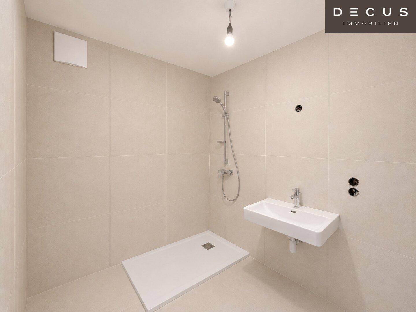 Unmöbliertes Badezimmer mit Duschbereich und Wandwaschbecken, bereit für die Fertigstellung.