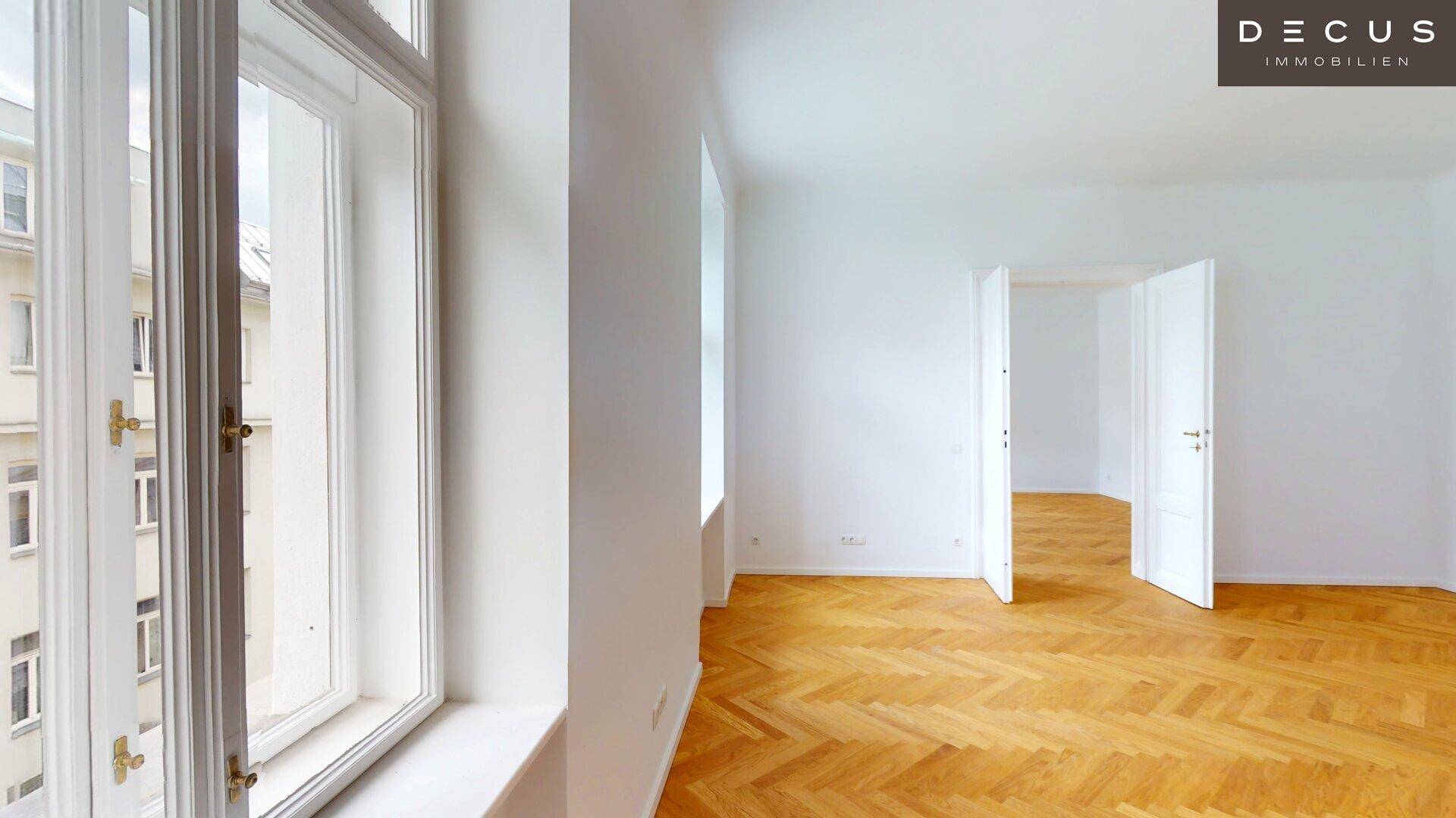 Detailansicht eines hohen Fensters in einem hellen Raum mit Fischgrätparkett und weiß gestrichenen Wänden.