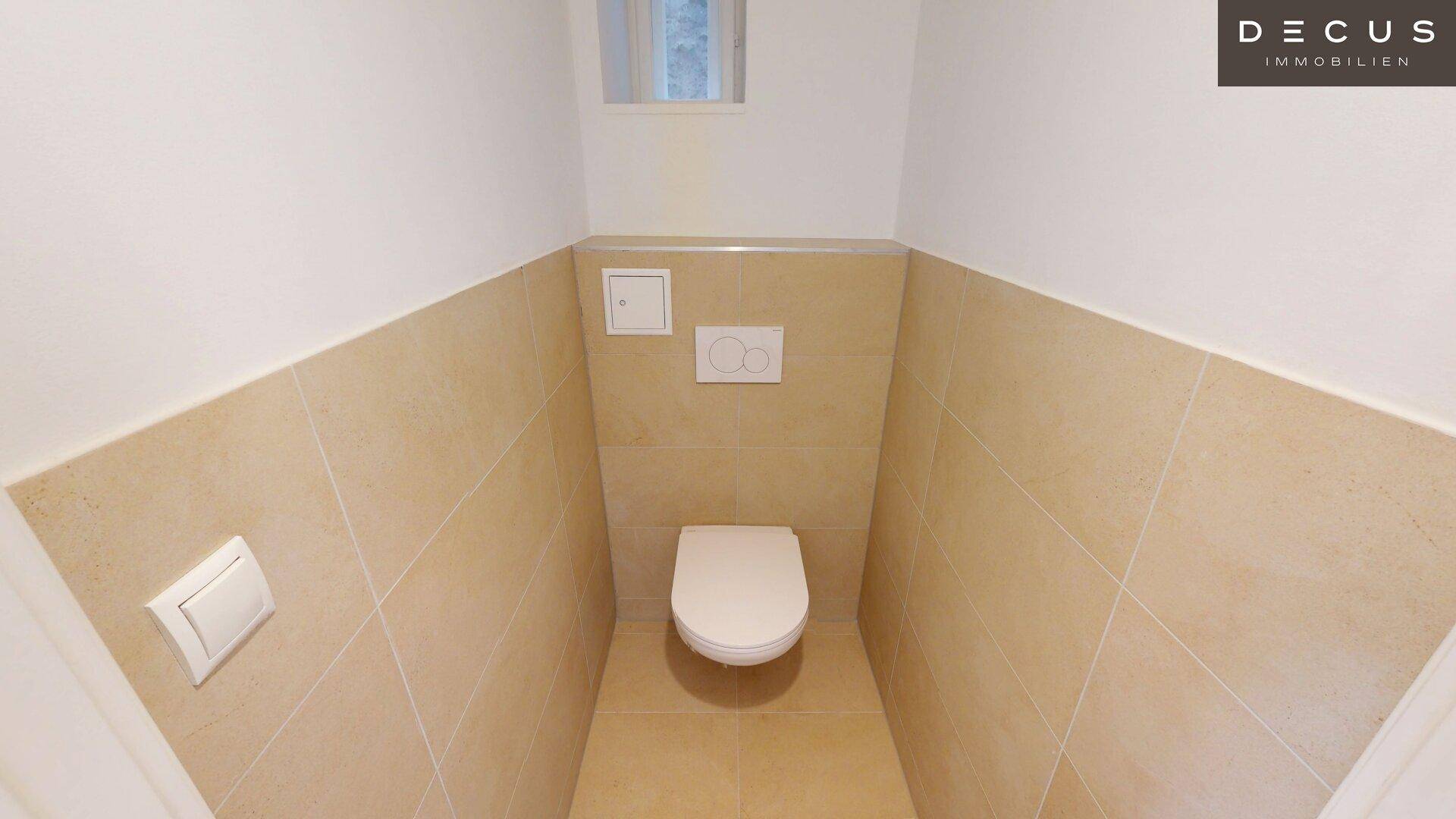 Separate Toilette mit beigefarbenen Fliesen und einem kleinen Fenster für Belüftung und Licht.