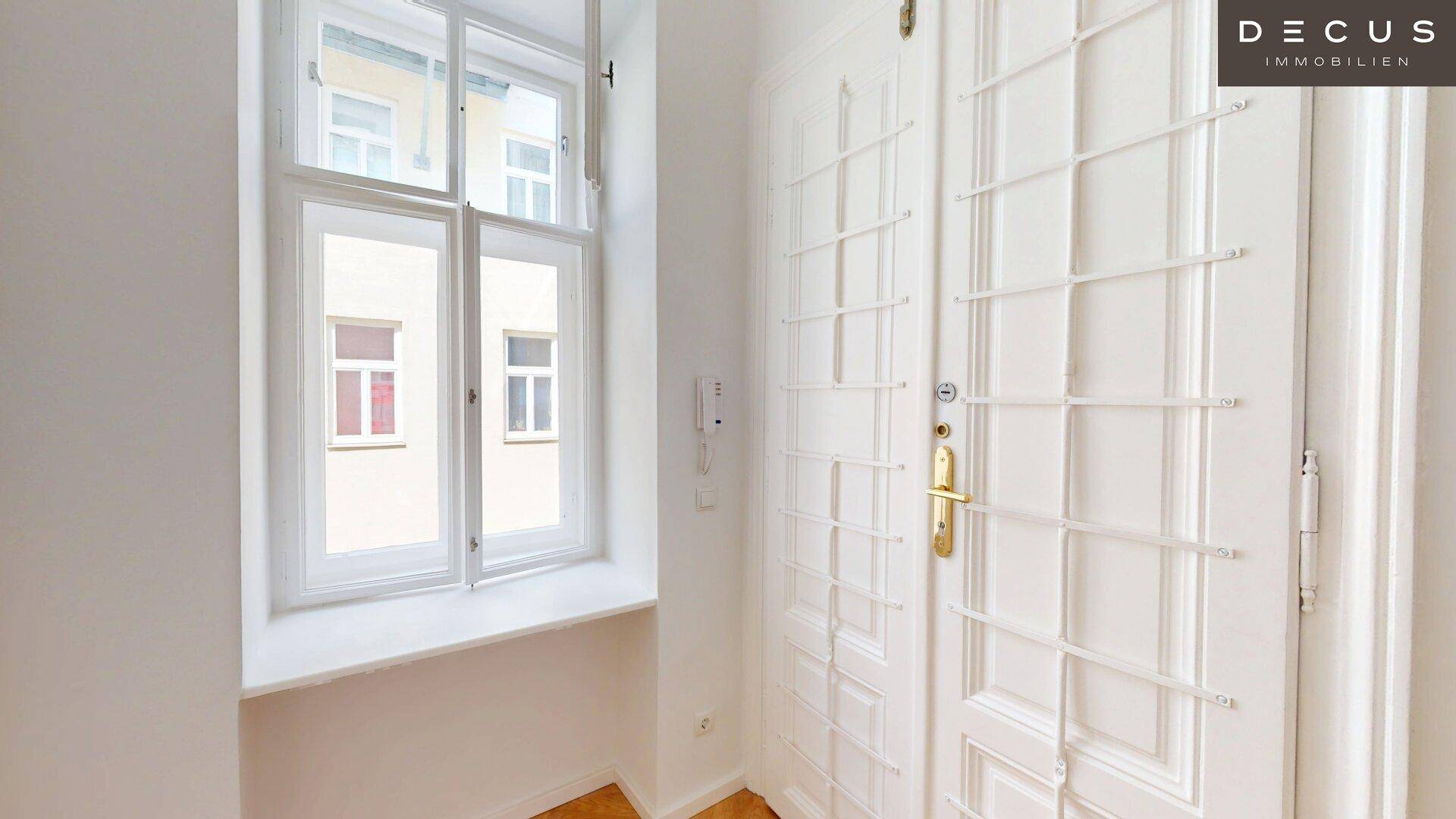 Heller Eingangsbereich mit Fischgrätparkett, einer weißen Eingangstür und einem hohen Fenster.