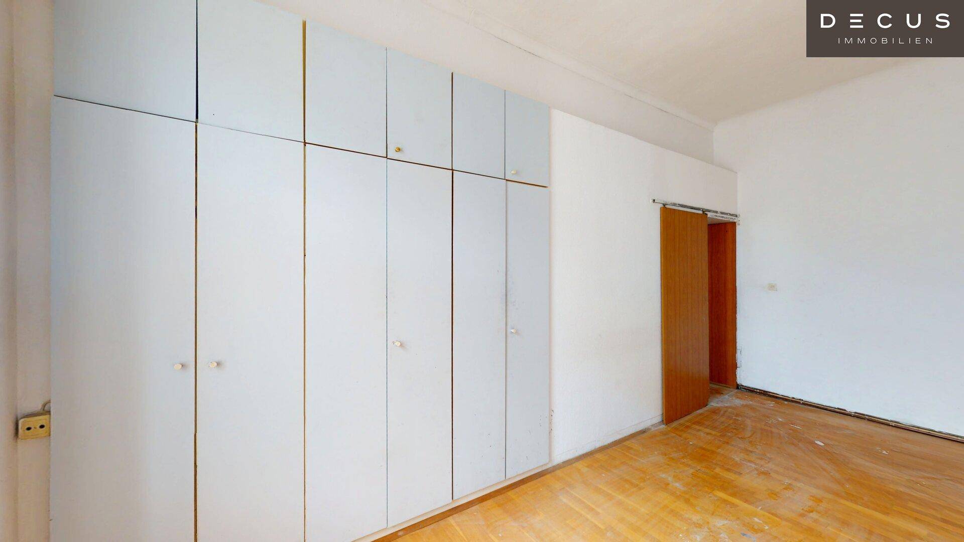 Schlafzimmer mit Parkettboden und einer Wand voller Einbauschränke.