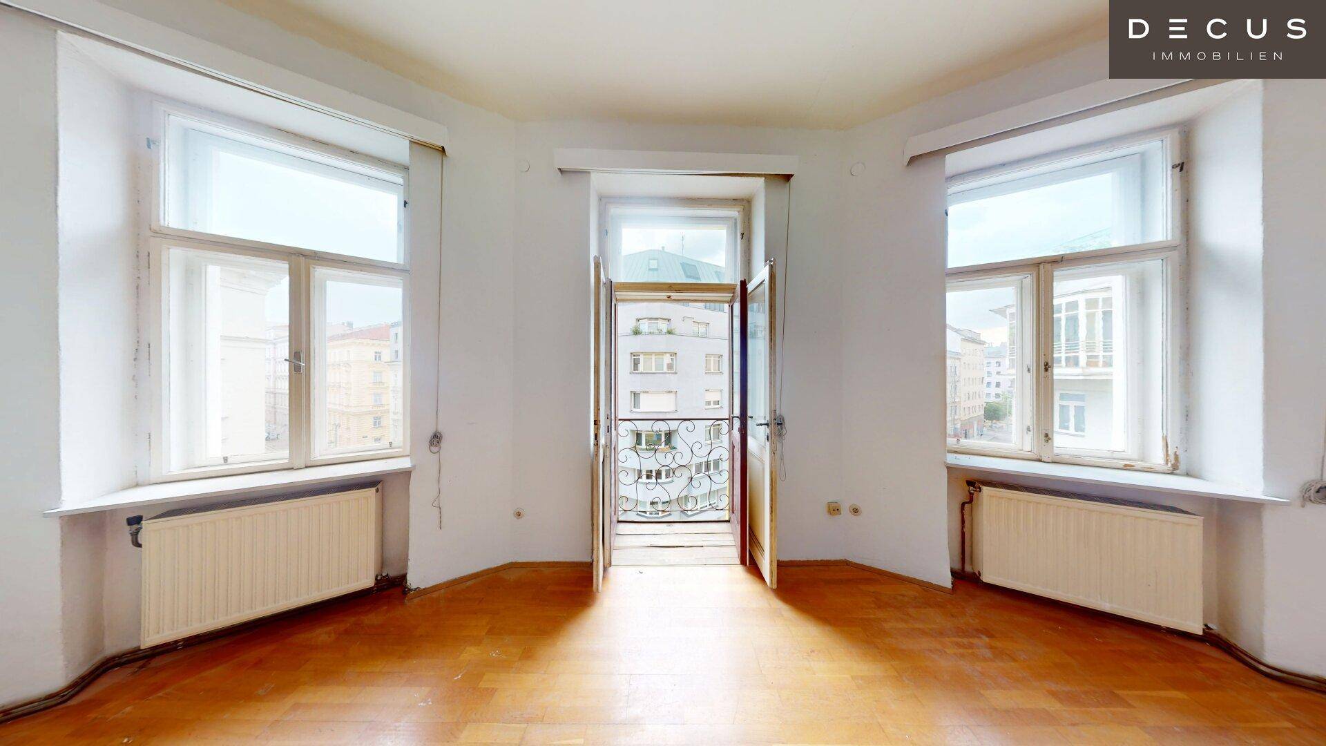 Helles Zimmer mit französischem Balkon, Parkettboden und Blick auf die Stadt.