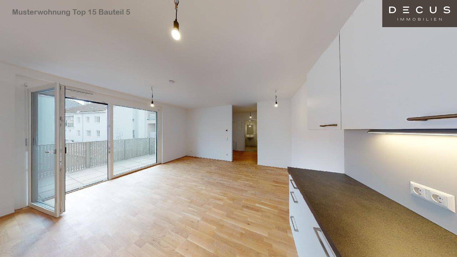Geräumiger Wohnbereich mit Holzboden, Zugang zum Balkon und Blick auf die moderne Küchenzeile.