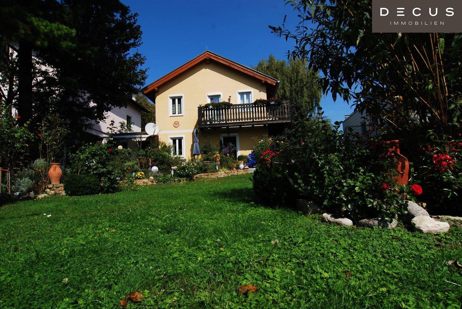 Charmantes Einfamilienhaus mit Balkon und gepflegtem Vorgarten unter blauem Himmel.