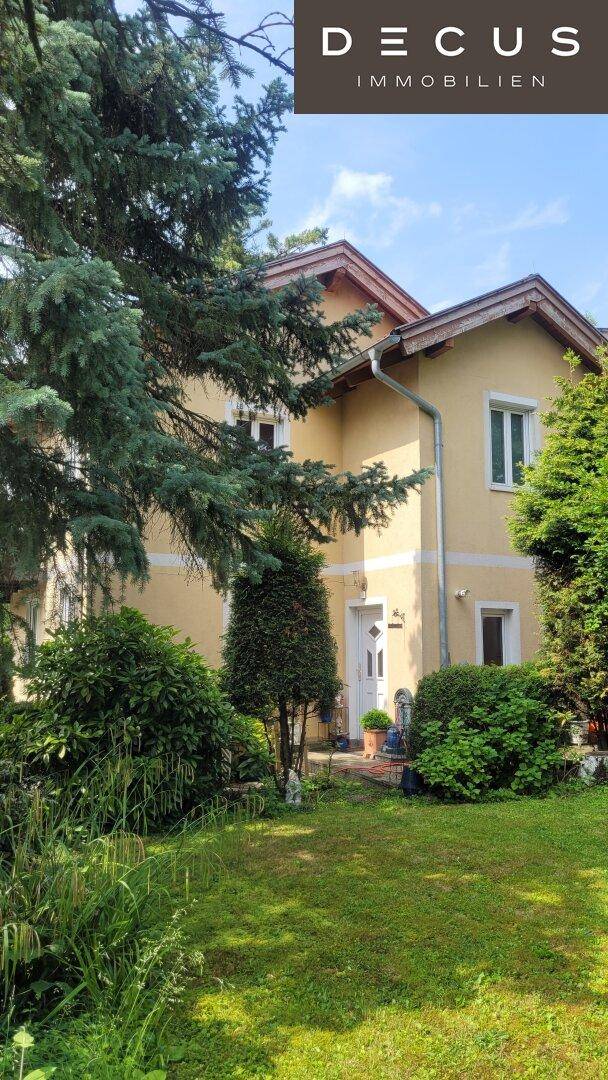 Vorderansicht des Hauses mit Eingangsbereich, umgeben von grünen Bäumen und Sträuchern.