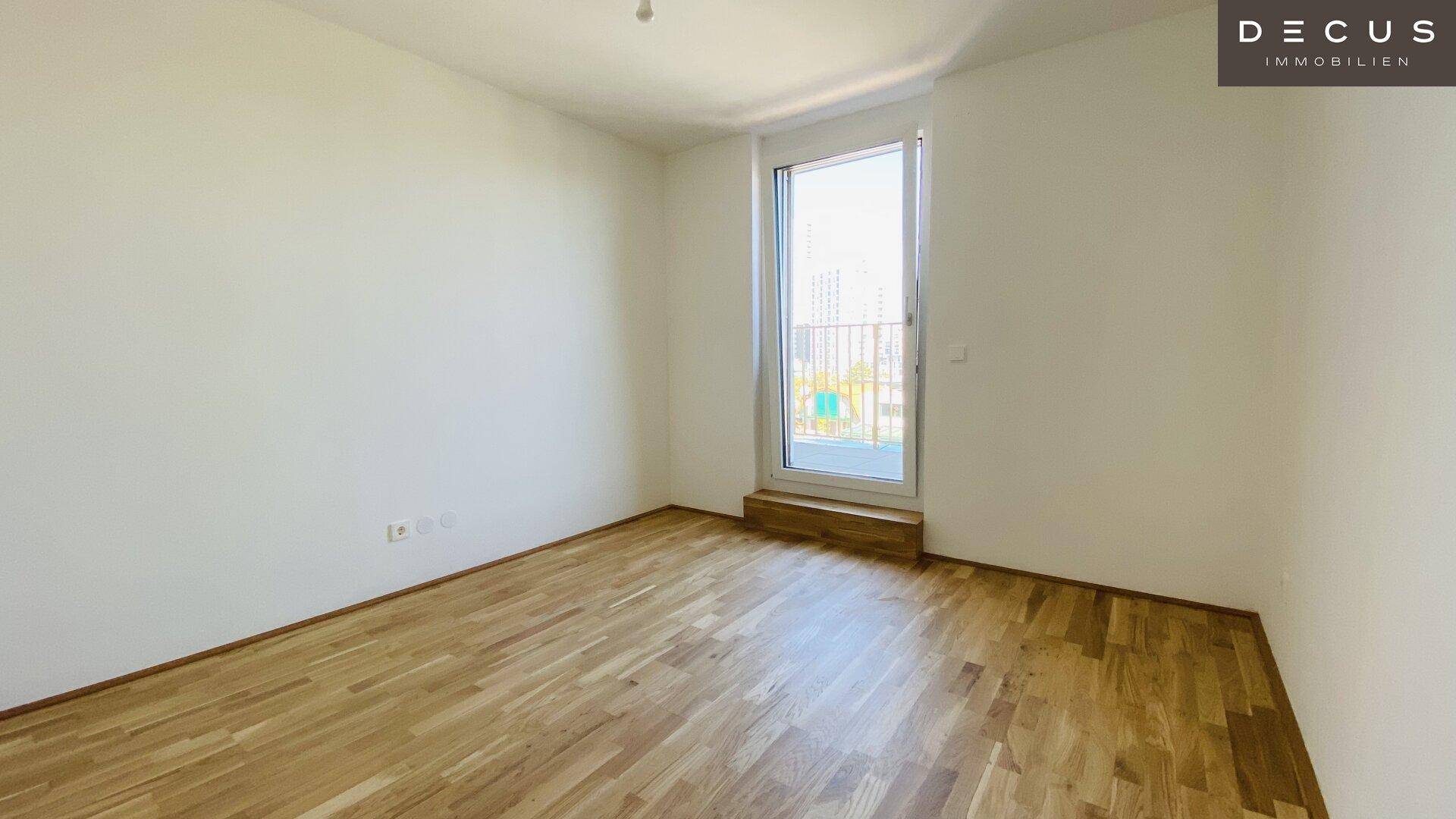 Helles Schlafzimmer mit Parkettboden und Zugang zu einem französischen Balkon.