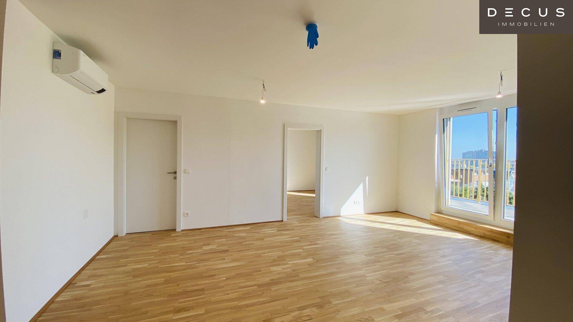 Geräumiger Wohnbereich mit Parkettboden, Klimaanlage und großem Fenster mit Balkonzugang.