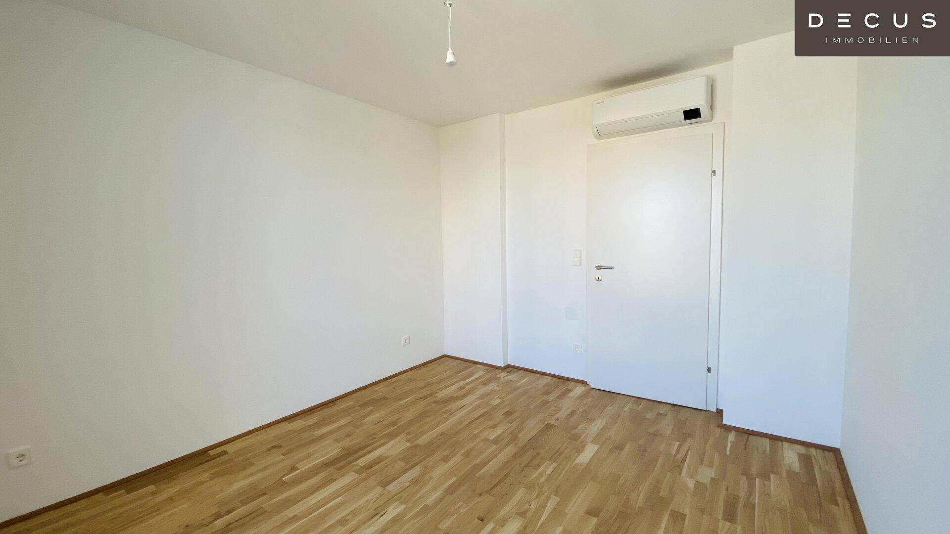 Helles Zimmer mit Parkettboden, Klimaanlage und weiß gestrichenen Wänden.