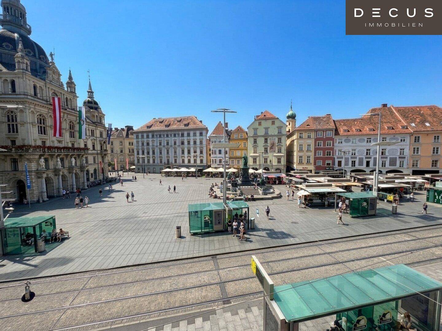 Historischer Stadtplatz mit belebten Cafés, Gebäuden und Straßenbahnschienen an einem sonnigen Tag.