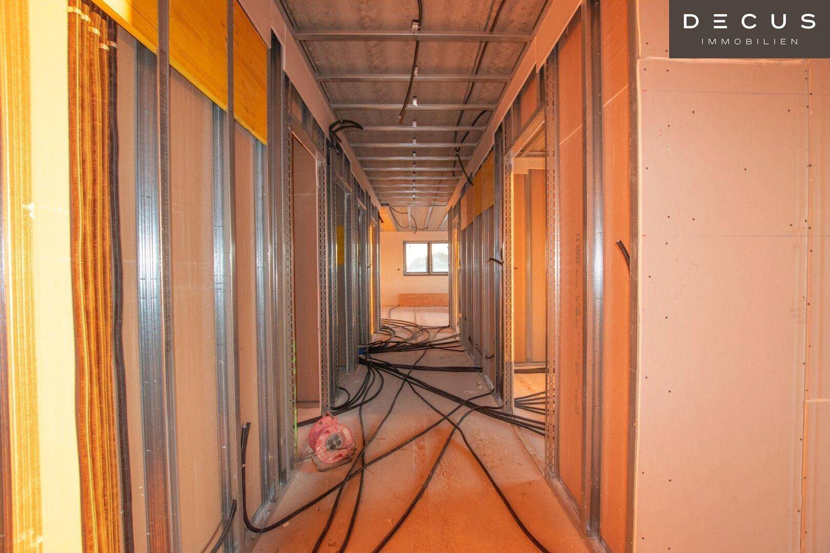 Flur im Rohbau mit sichtbaren Trockenbauwänden und Elektroverkabelung.