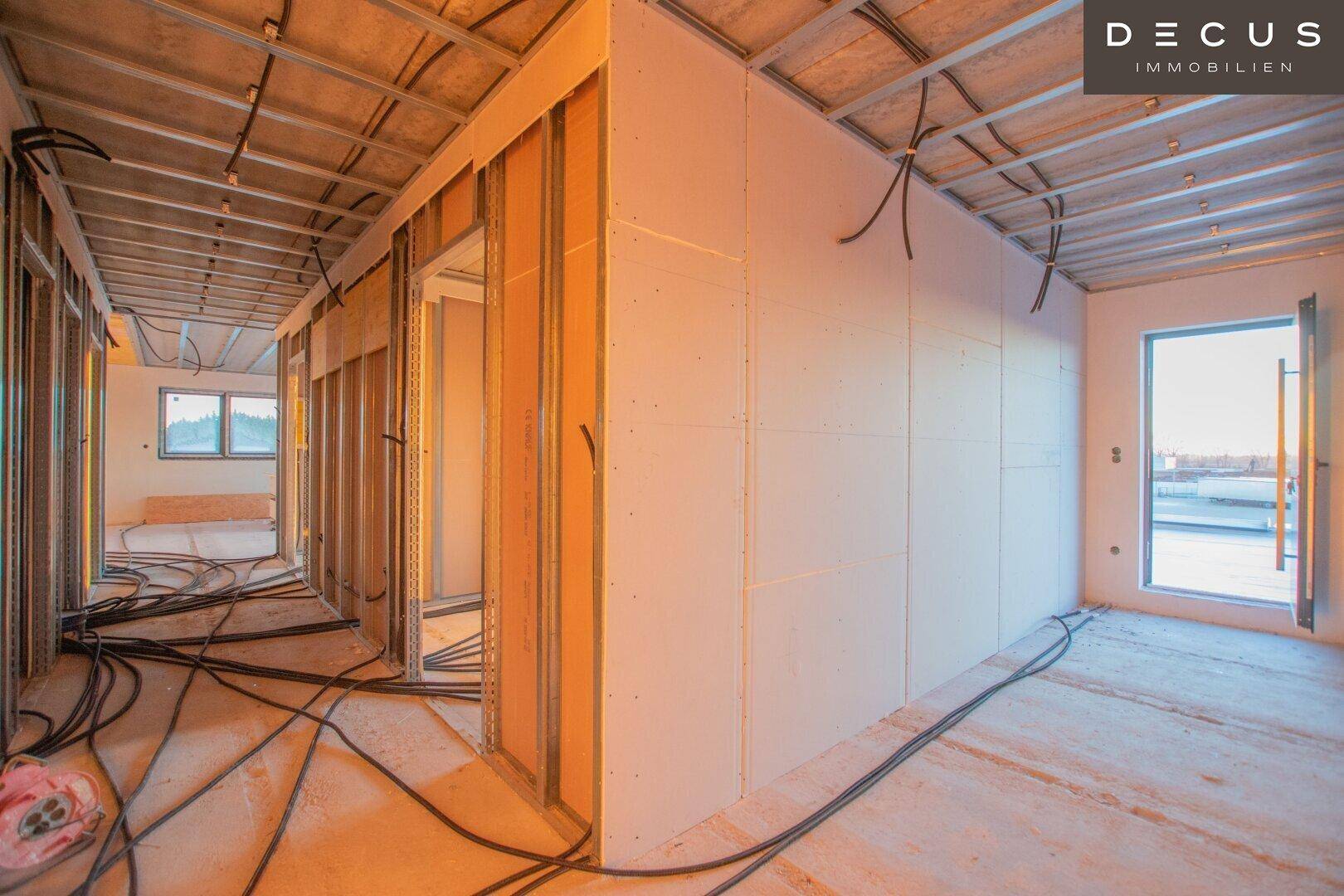 Innenraum im Rohbau mit Trockenbauwänden und Blick nach draußen.