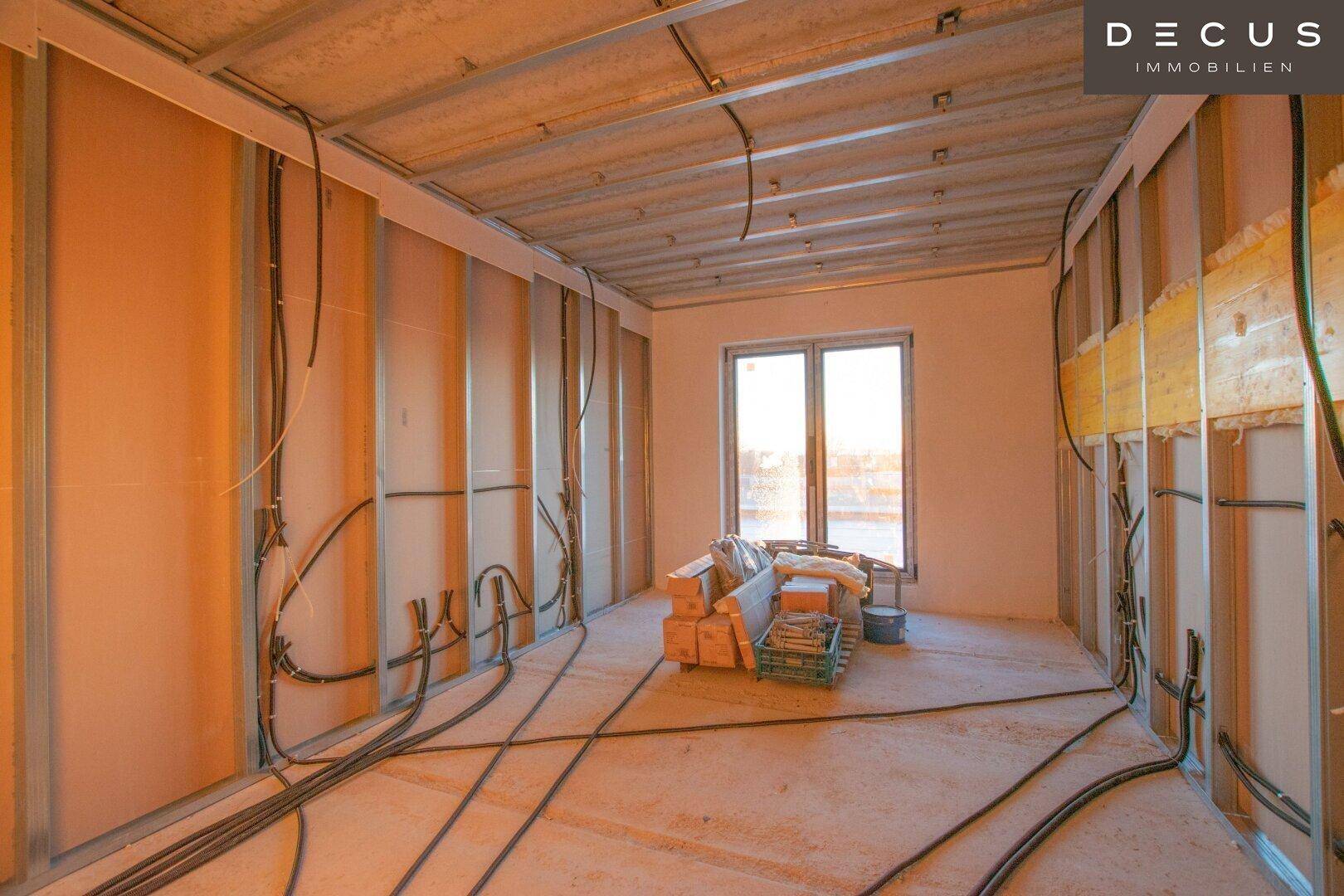 Raum im Rohbau mit Fenster und sichtbaren Installationen für den Innenausbau.