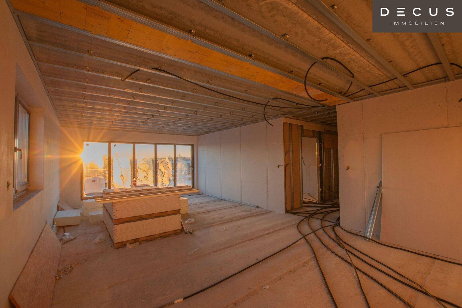 Rohbauzimmer mit großen Fenstern und Blick auf den Sonnenuntergang.
