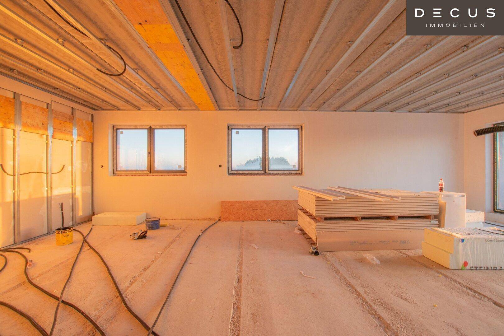 Großer Raum im Rohbau mit mehreren Fenstern und Baumaterialien.