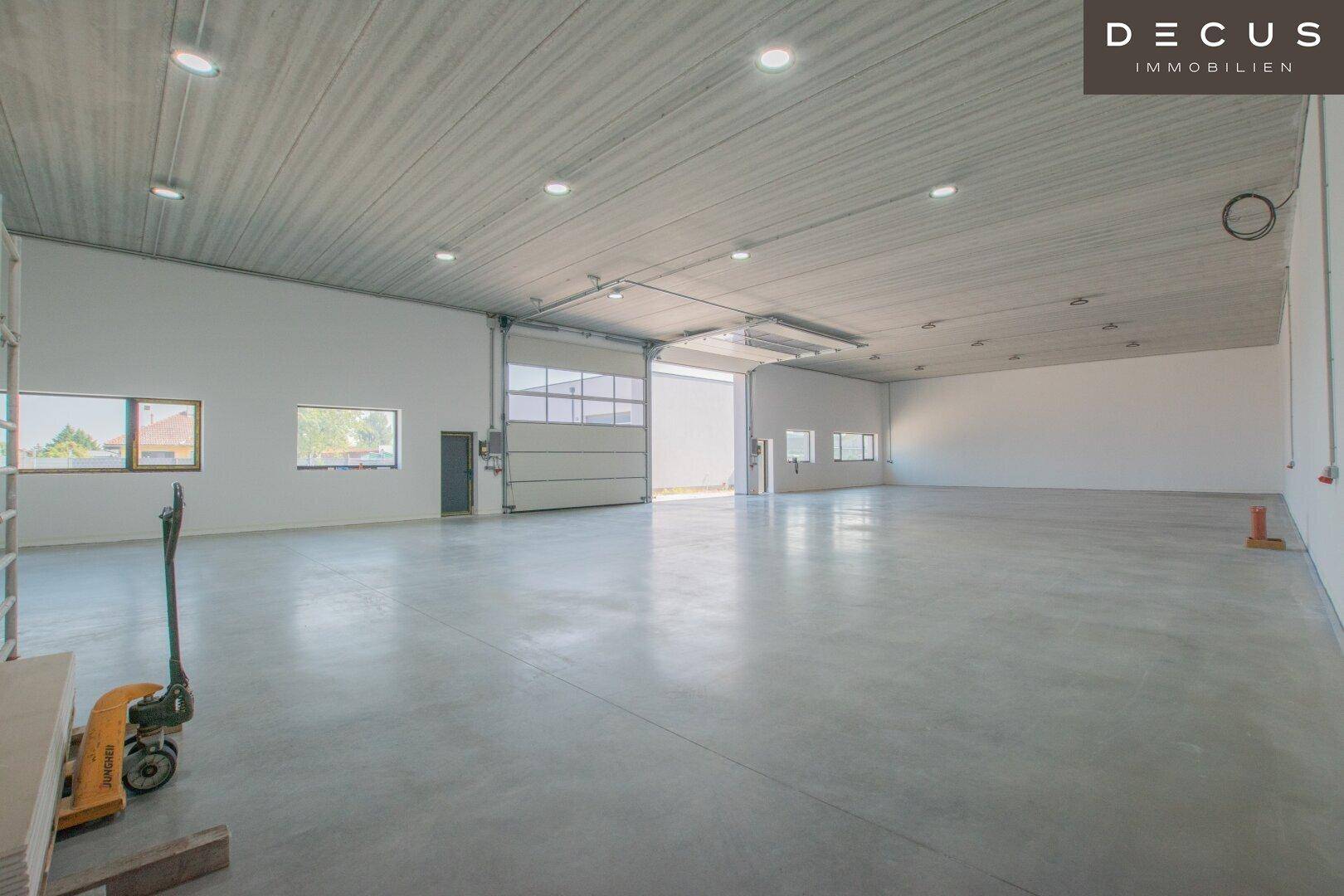 Große, leere Lagerhalle mit Betonboden und Deckenbeleuchtung.