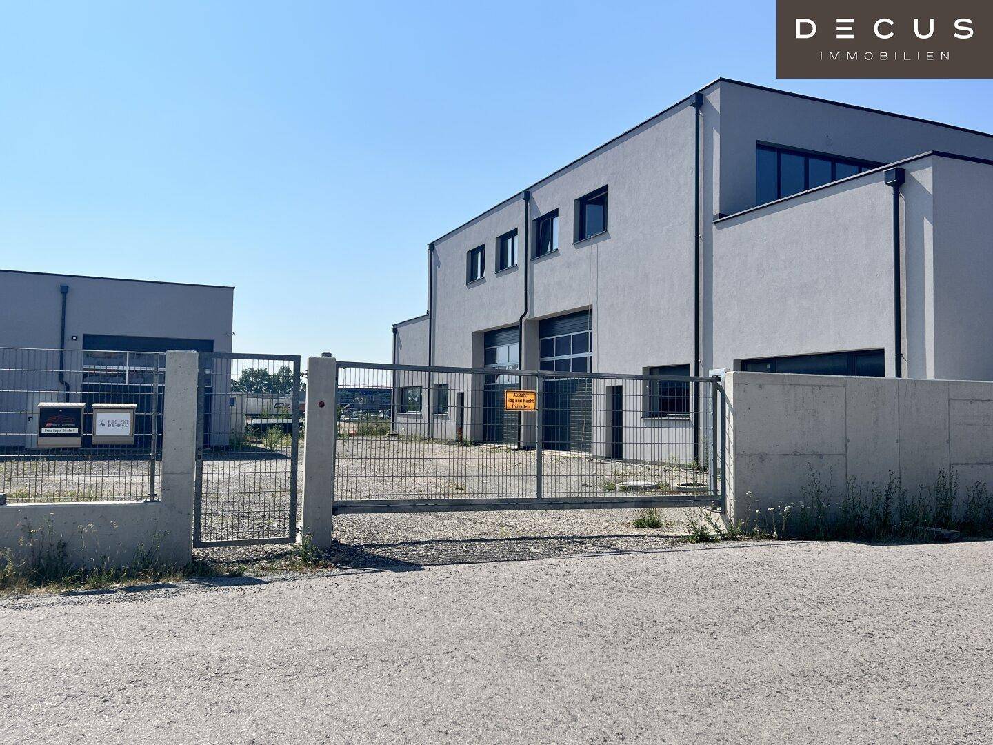 Ansicht des modernen Gewerbegebäudes mit Zufahrtstor und umzäuntem Vorplatz.