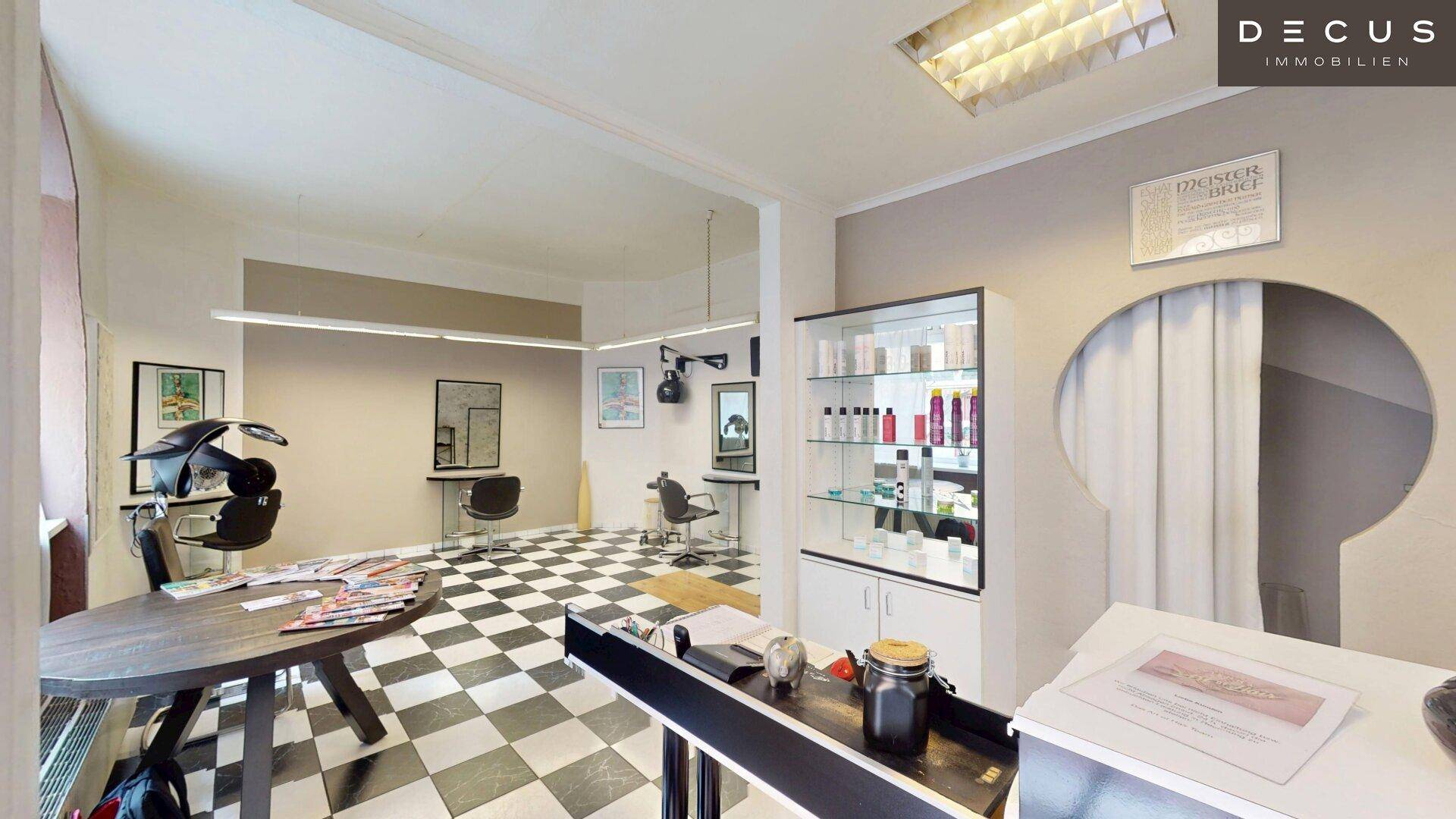 Wartebereich und Styling-Stationen in einem Friseursalon mit schwarz-weißem Fliesenboden.
