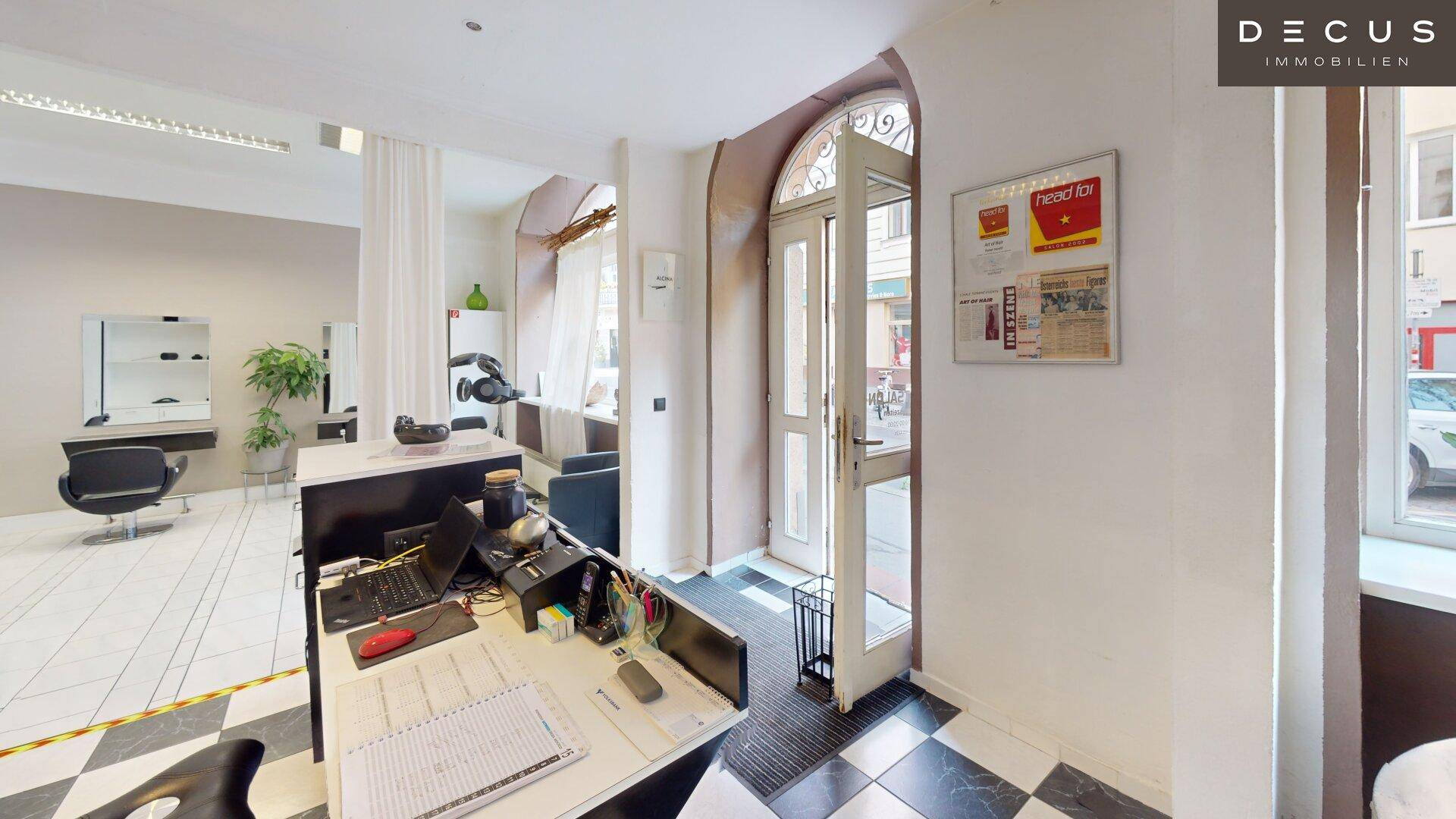 Empfangsbereich eines Friseursalons mit Theke und offener Eingangstür zur Straße.