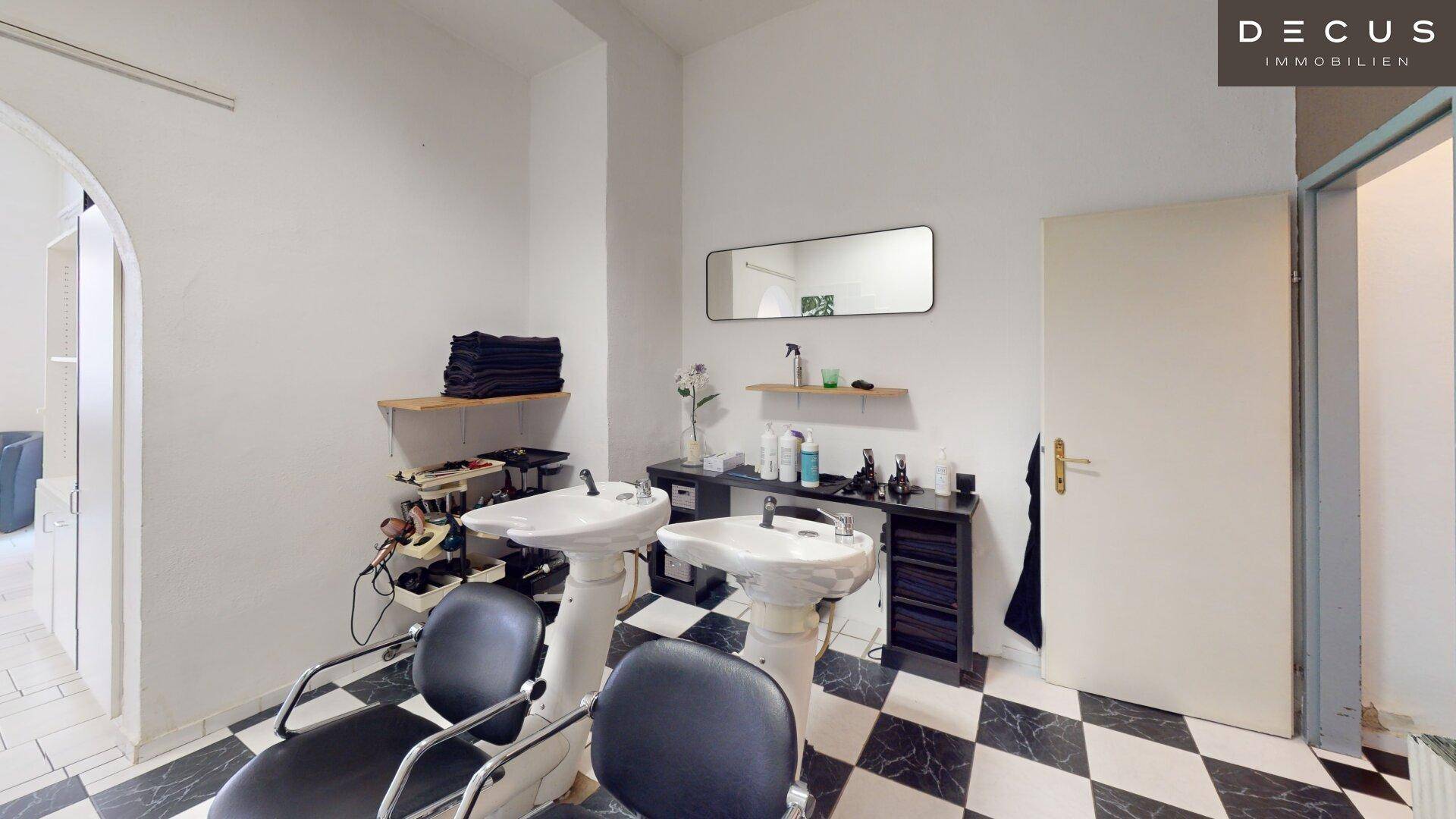 Waschbereich im Friseursalon mit zwei Haarwaschbecken, Spiegel und Zugang zu einem Nebenraum.