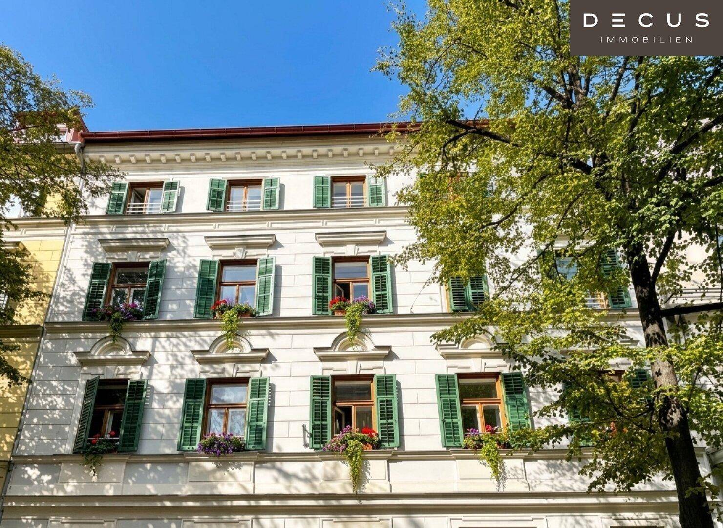 Klassische Fassade eines Altbaus mit grünen Fensterläden und Blumenkästen unter strahlend blauem Himmel.