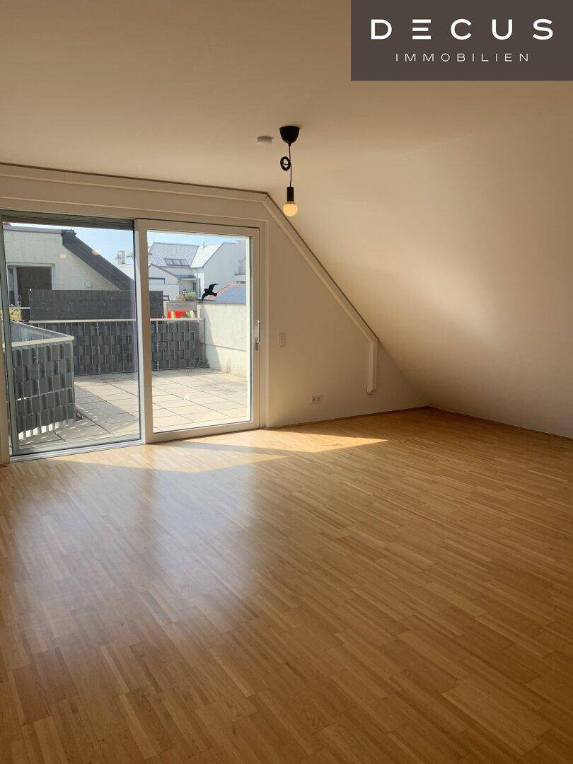 Helles Wohnzimmer mit Dachschräge, Parkettboden und Zugang zu einer sonnigen Terrasse.